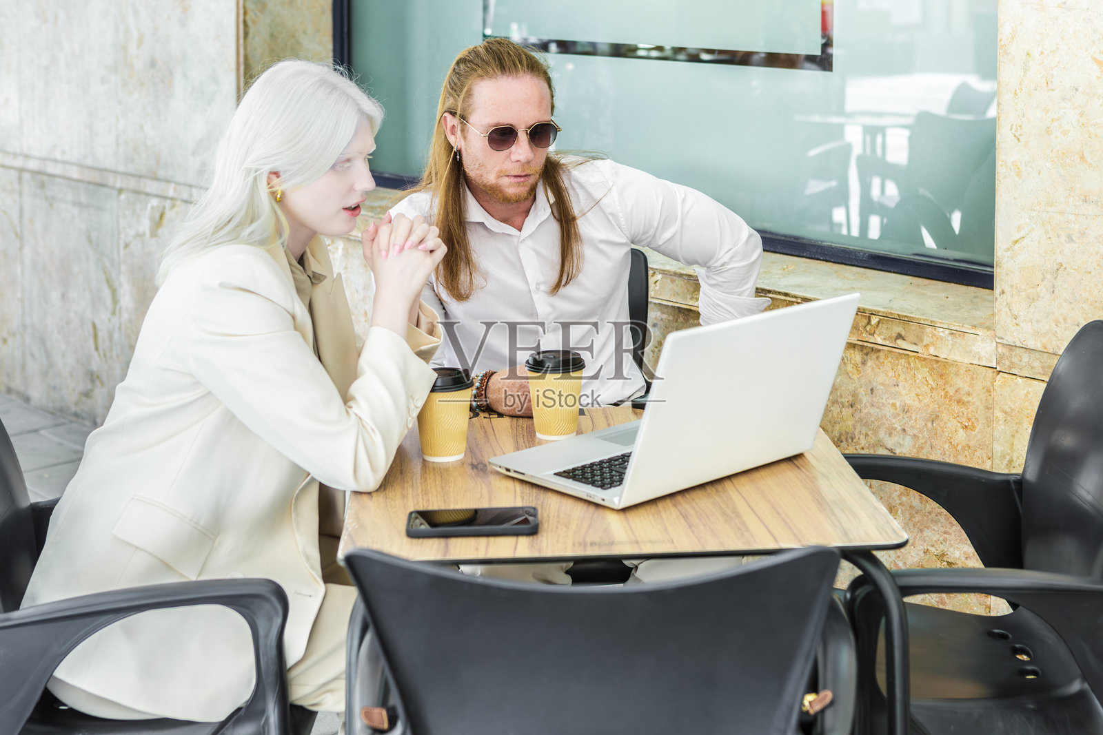 姜男与白化病女性在咖啡馆相遇,桌上有笔记本电脑和咖啡。照片摄影图片
