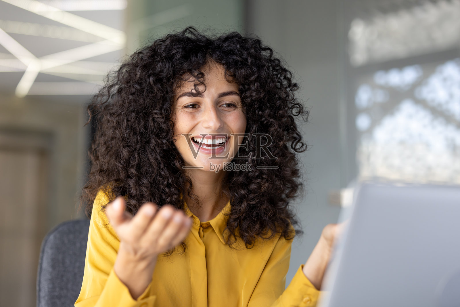 一位迷人的卷发女性在与同事的视频会议中欢笑互动。照片摄影图片