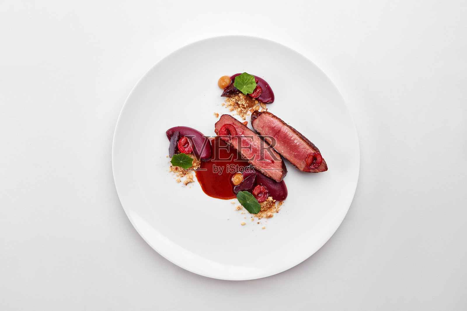 一盘精致的美食,完美烹饪的鸭胸肉配樱桃、浓郁的酱汁和脆皮,前景中搭配一杯红酒。照片摄影图片