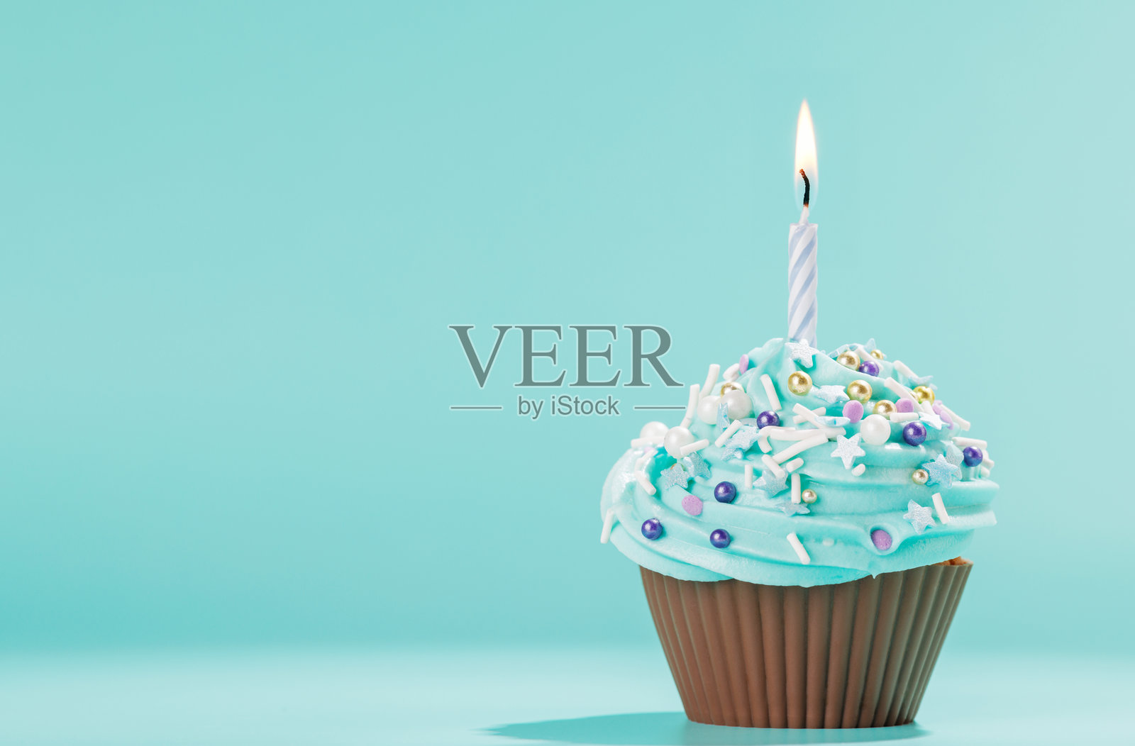 节日杯子蛋糕,上面装饰着旋转的糖霜和一根点燃的蜡烛照片摄影图片