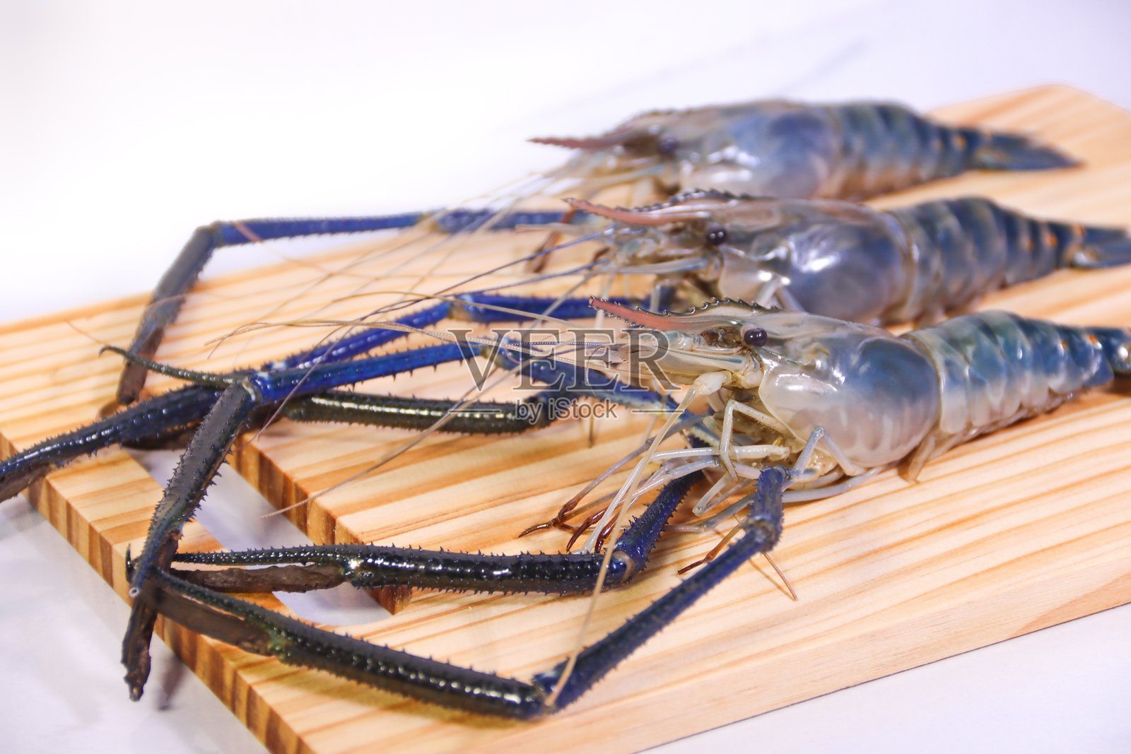 三只河虾斜放在松木砧板上照片摄影图片