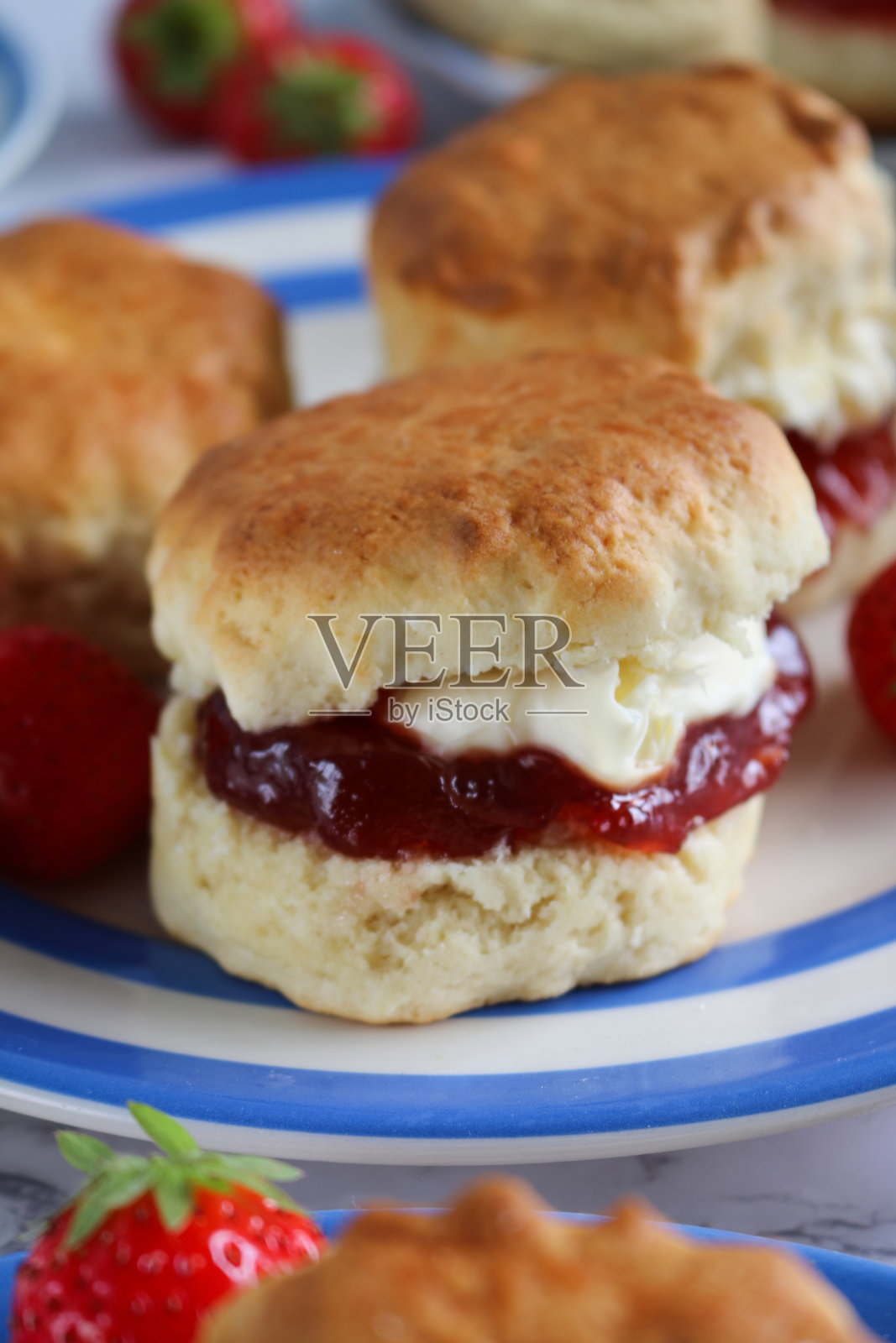 蓝白条纹的康沃尔陶瓷盘上放着草莓酱和浓奶油的普通司康饼特写,旁边有草莓,传统英式下午茶,搭配果酱和奶油,体现康沃尔和德文郡的风格,社交辩论概念照片摄影图片