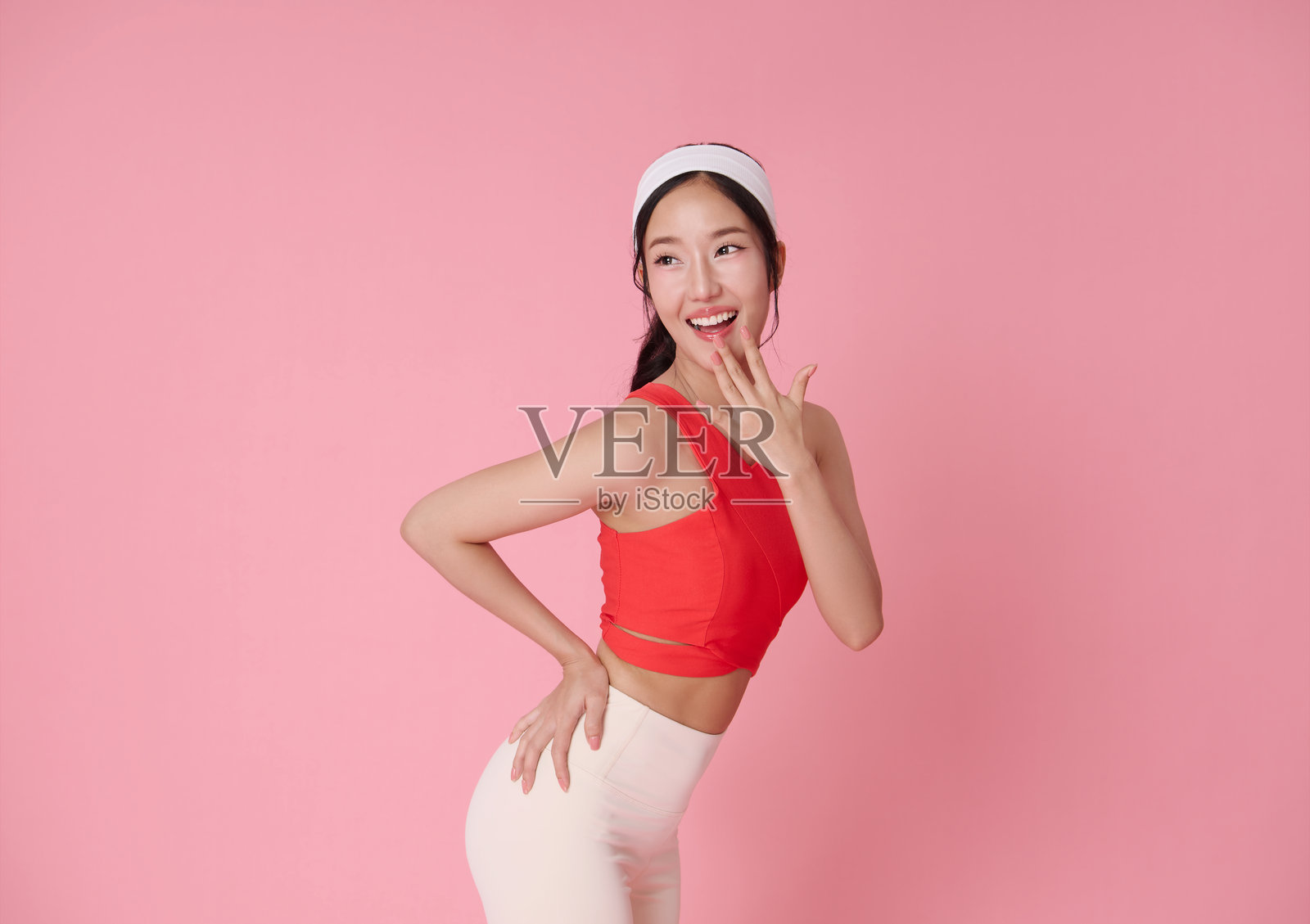 穿着红色运动上衣的亚洲女性健身模特在粉色背景上微笑,适合健康、积极生活方式和运动休闲广告,留有空白空间。照片摄影图片
