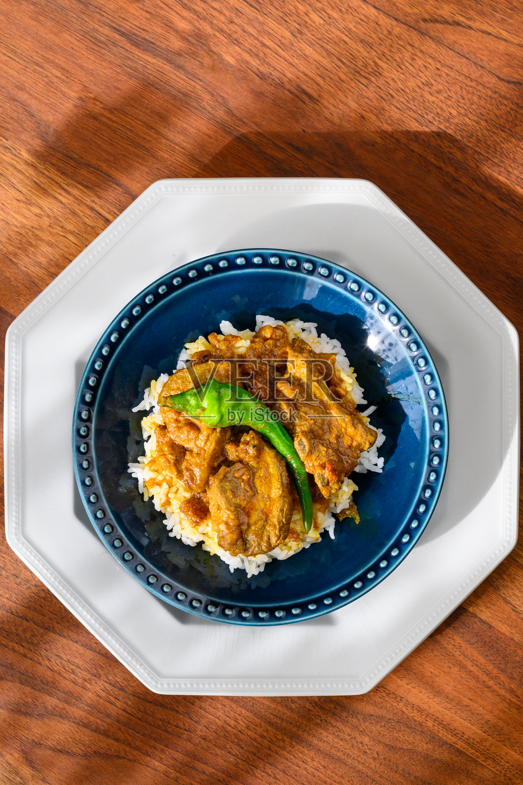 蓝色碗中的羊肉咖喱配米饭,放在古董胡桃木桌上照片摄影图片