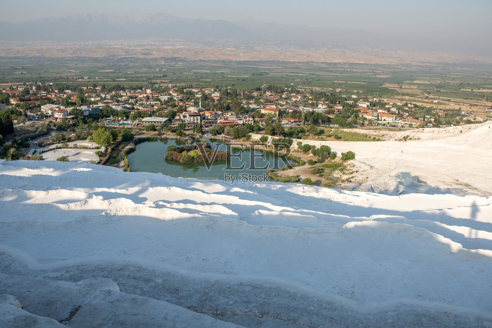 在阳光明媚的日子里,探索帕穆克卡莱令人惊叹的钙华 terraces,欣赏周围村庄和郁郁葱葱的自然风光。照片摄影图片