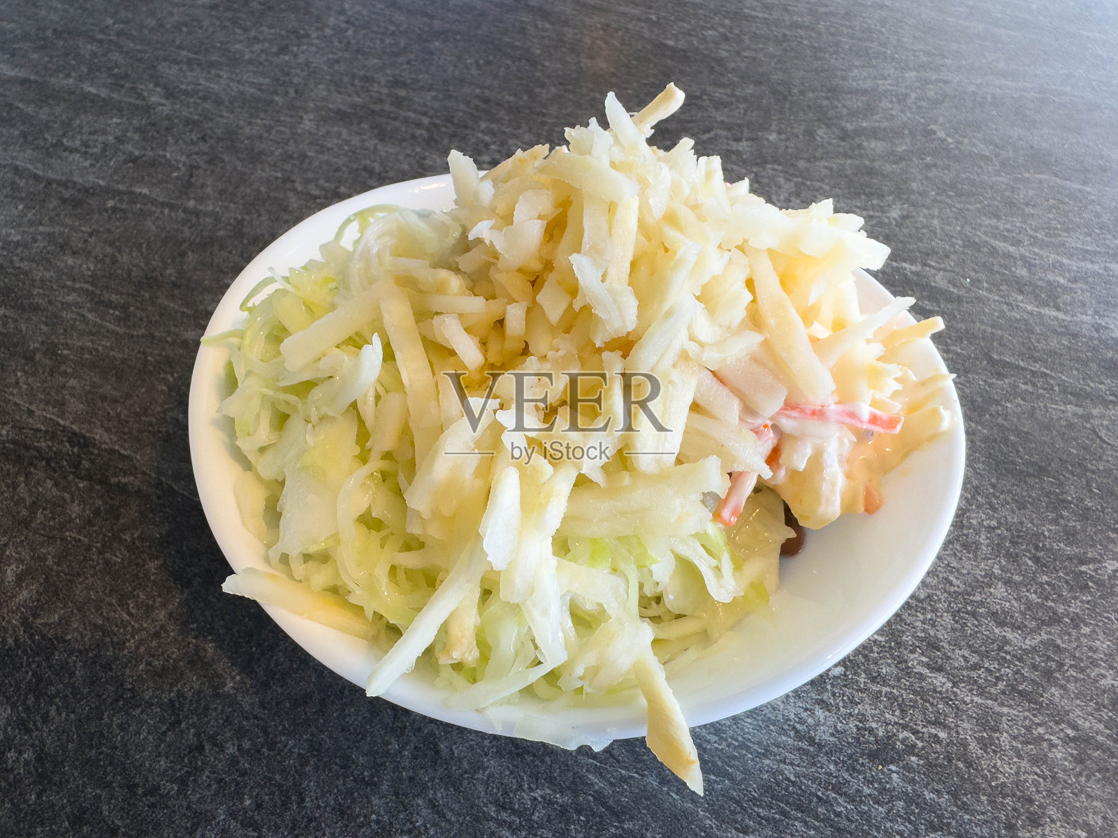 新鲜的卷心菜和苹果沙拉放在灰色表面的白色碗中照片摄影图片