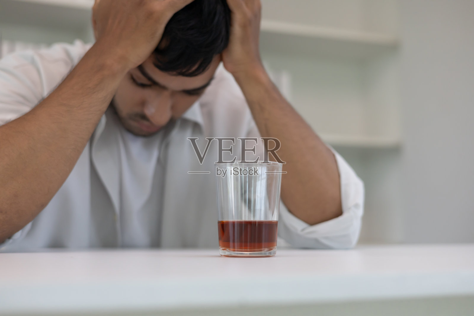 沮丧的年轻亚洲男子独自在家喝威士忌,感到痛苦,压力大,孤独,因酗酒而遭受生活和家庭问题的困扰。照片摄影图片