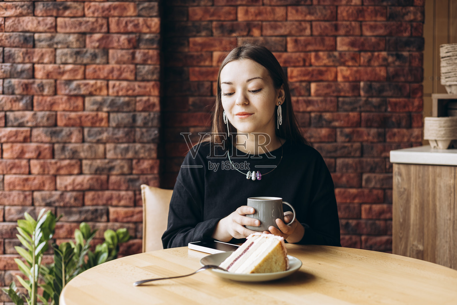 年轻女性在早晨咖啡馆场景中喝黑滤咖啡,旁边有蛋糕。照片摄影图片
