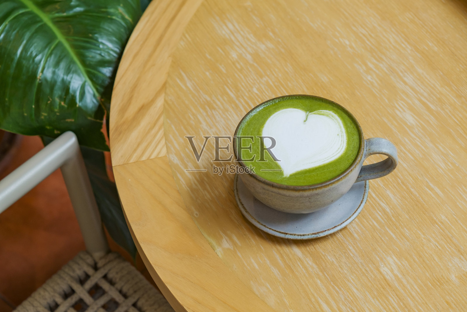 甜美的热抹茶拿铁心形拉花放在木桌上,角落里装饰着绿色植物。照片摄影图片