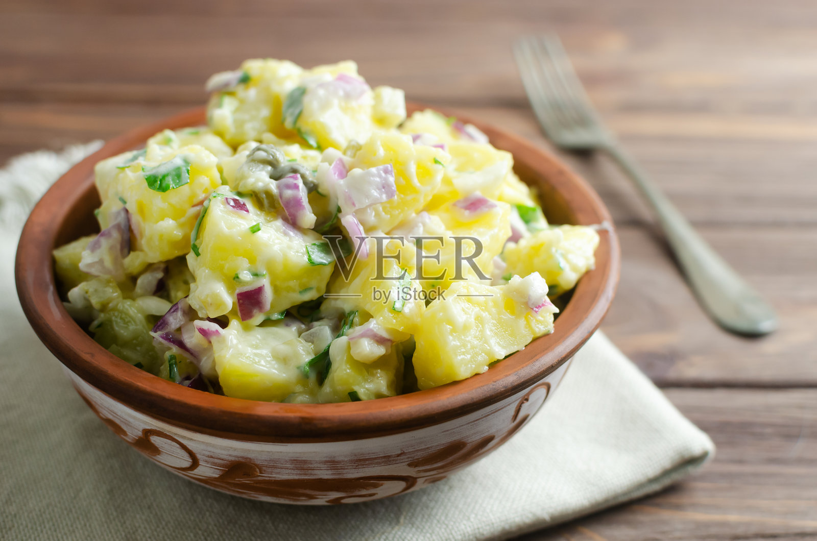 紫洋葱、腌黄瓜和香菜的冷土豆沙拉,盛放在木桌上的陶瓷碗中。传统德国菜概念。乡村风格。选择性焦点。横向构图。留白。照片摄影图片