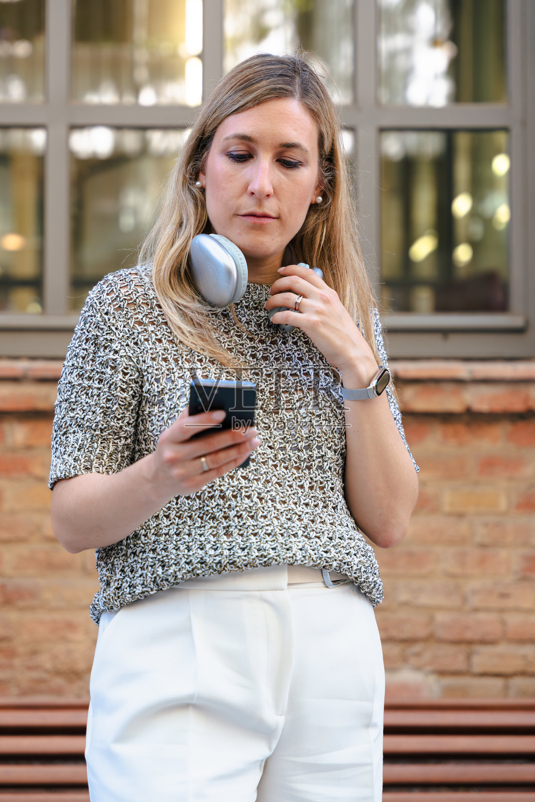 年轻女性在户外长椅上使用智能手机,戴着耳机微笑照片摄影图片