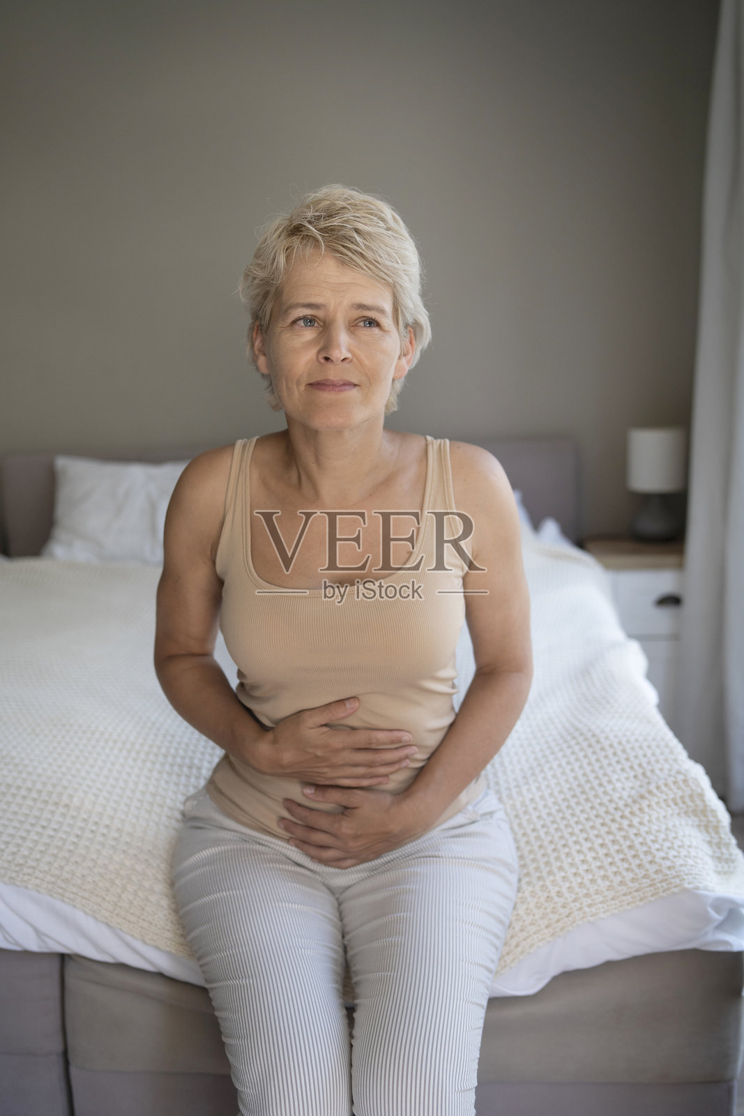 家中,女人坐在卧室里,感到腹部绞痛和恶心,正在忍受痛苦和疾病。照片摄影图片