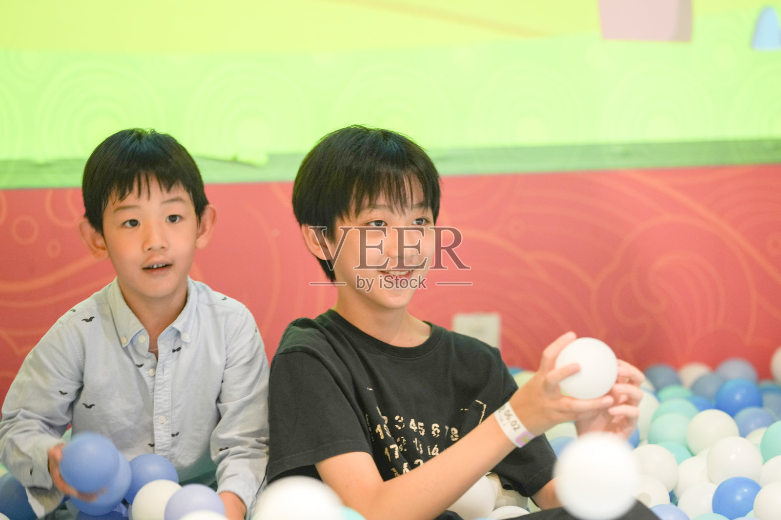 两个中国男孩和一个女孩在室内游乐区的塑料球池中玩耍。中国上海虹口区。春天。照片摄影图片