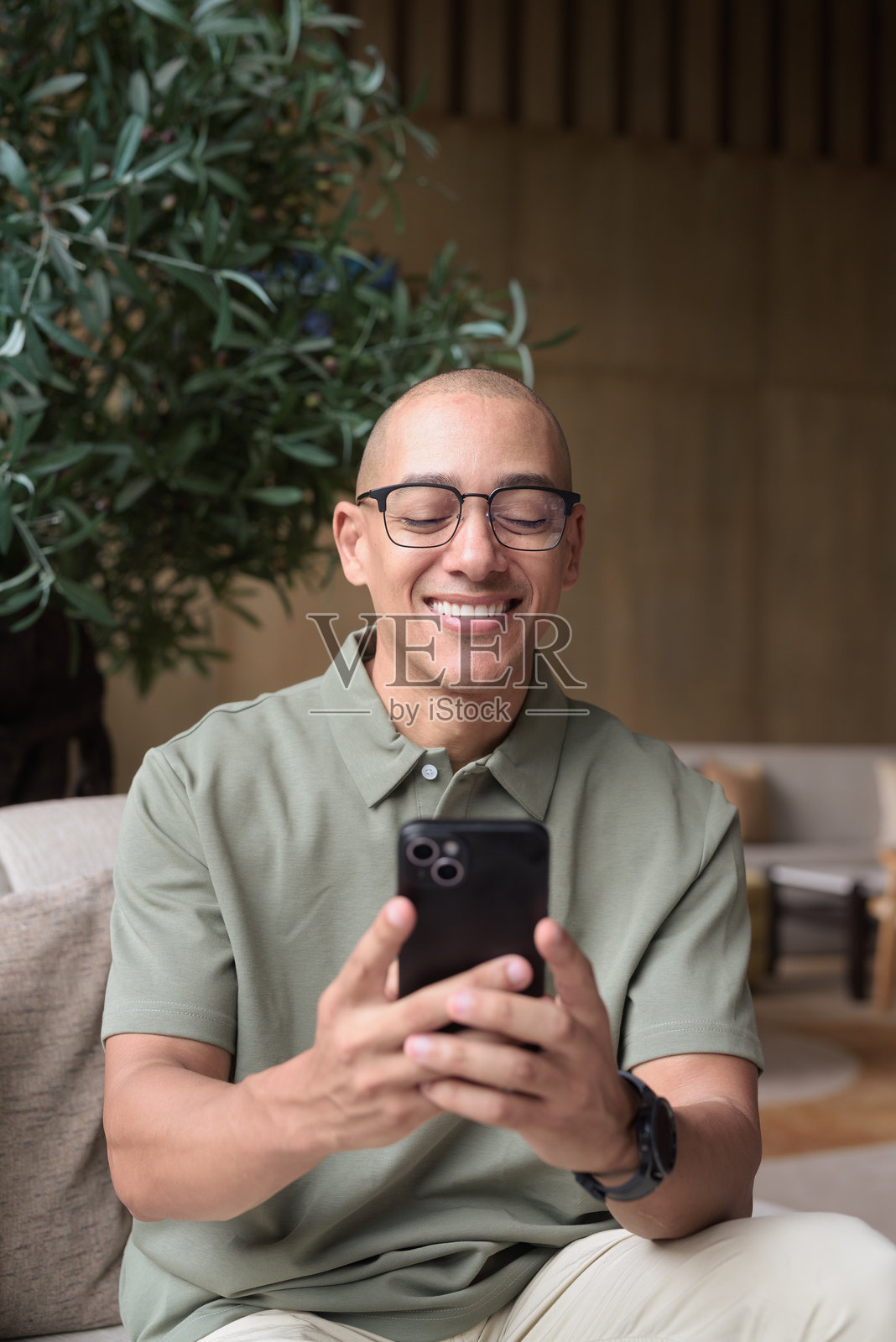 拉丁裔秃头男士在酒店休息室咖啡厅使用智能手机,展现商务休闲生活方式与沟通。照片摄影图片