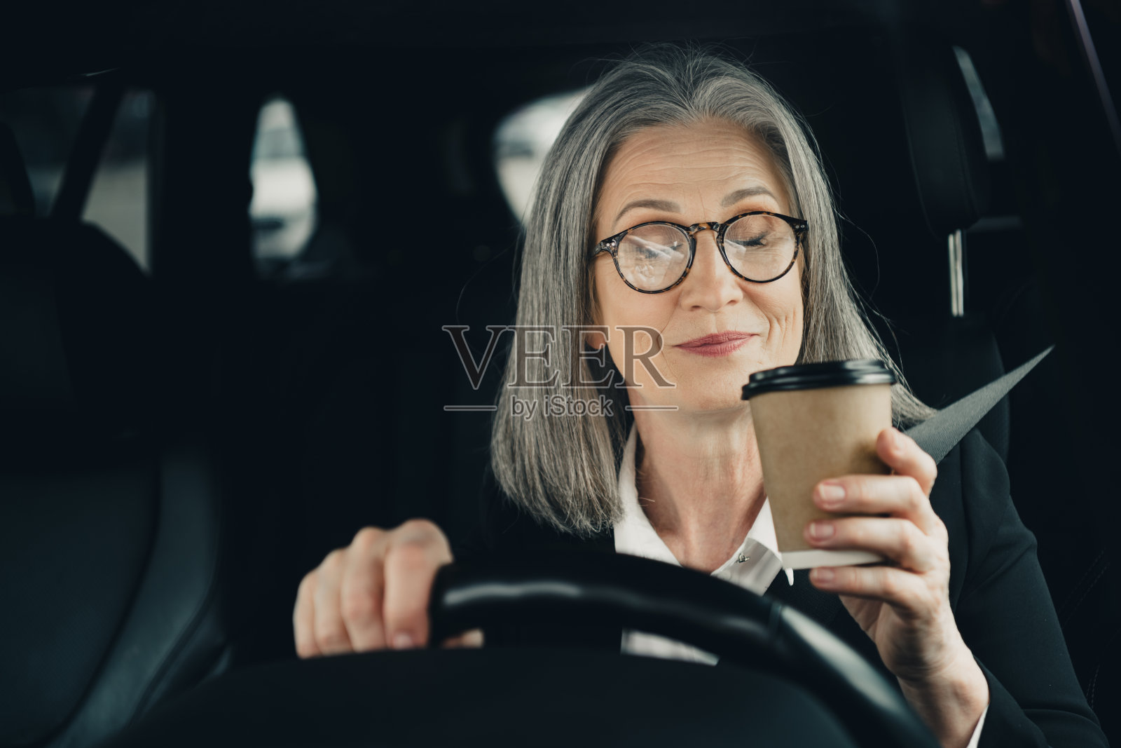 优雅的成熟的女商人戴着眼镜,在城市的白天穿着时尚的正装,享受着车内的咖啡。照片摄影图片