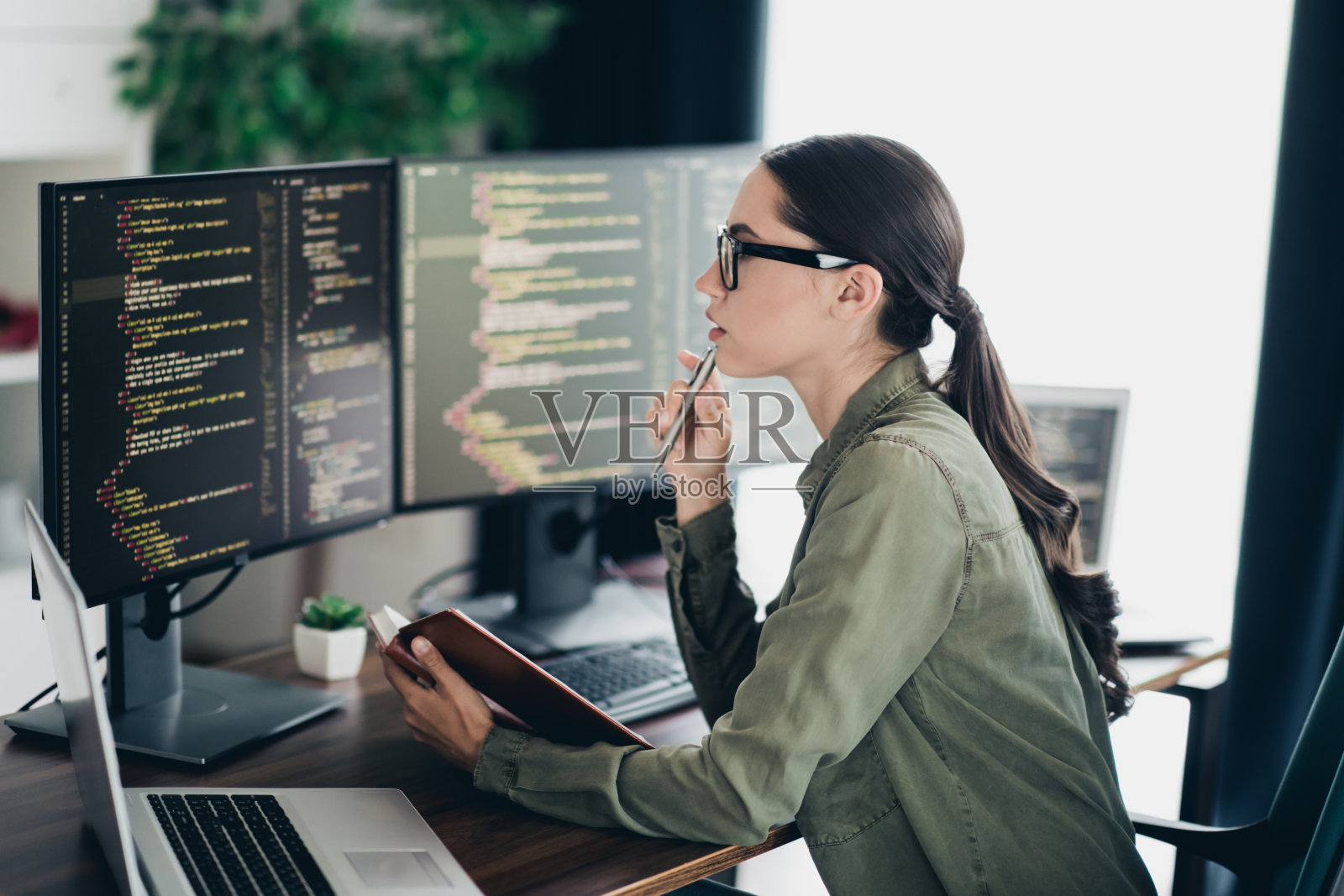 专注的年轻女性程序员在整洁的办公室空间中使用笔记本电脑分析代码照片摄影图片