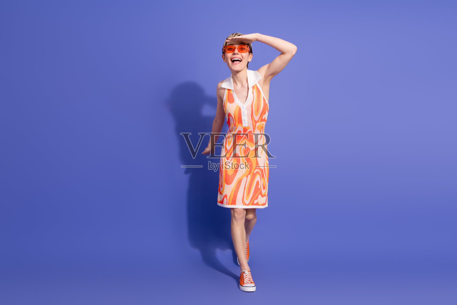 充满活力的年轻女性穿着复古夏季连衣裙,愉快地在鲜艳的紫色背景前摆姿势,散发着快乐的气息照片摄影图片