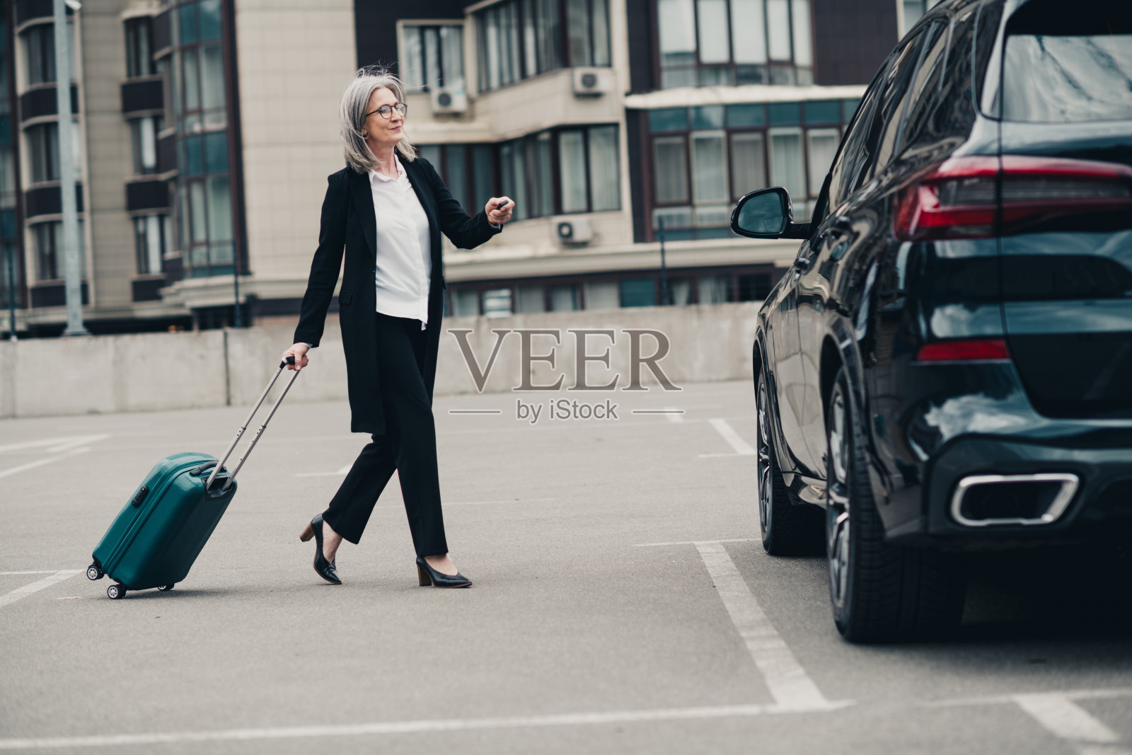 优雅的女商人提着行李箱,在白天的城市环境中走向一辆现代汽车照片摄影图片