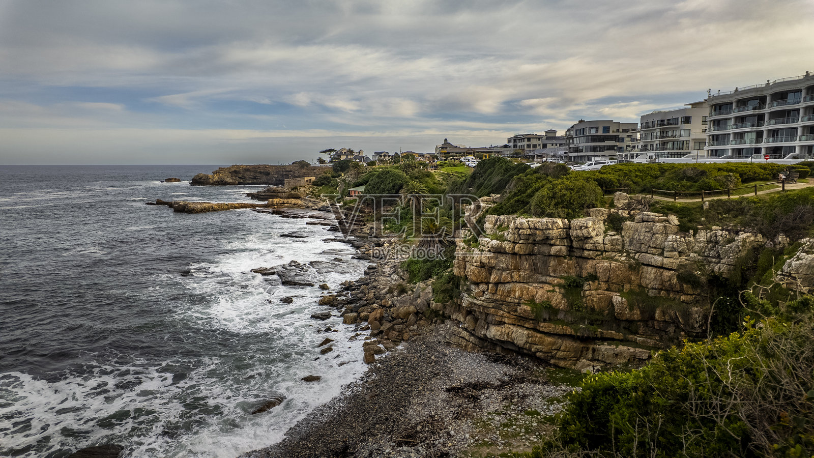 赫尔曼努斯海滨沿悬崖步道的壮丽景色,展示了戏剧性的岩石海岸线、旧港口、吉尔林斯角、豪华公寓以及南非鲸鱼海岸的郁郁葱葱的绿地。照片摄影图片