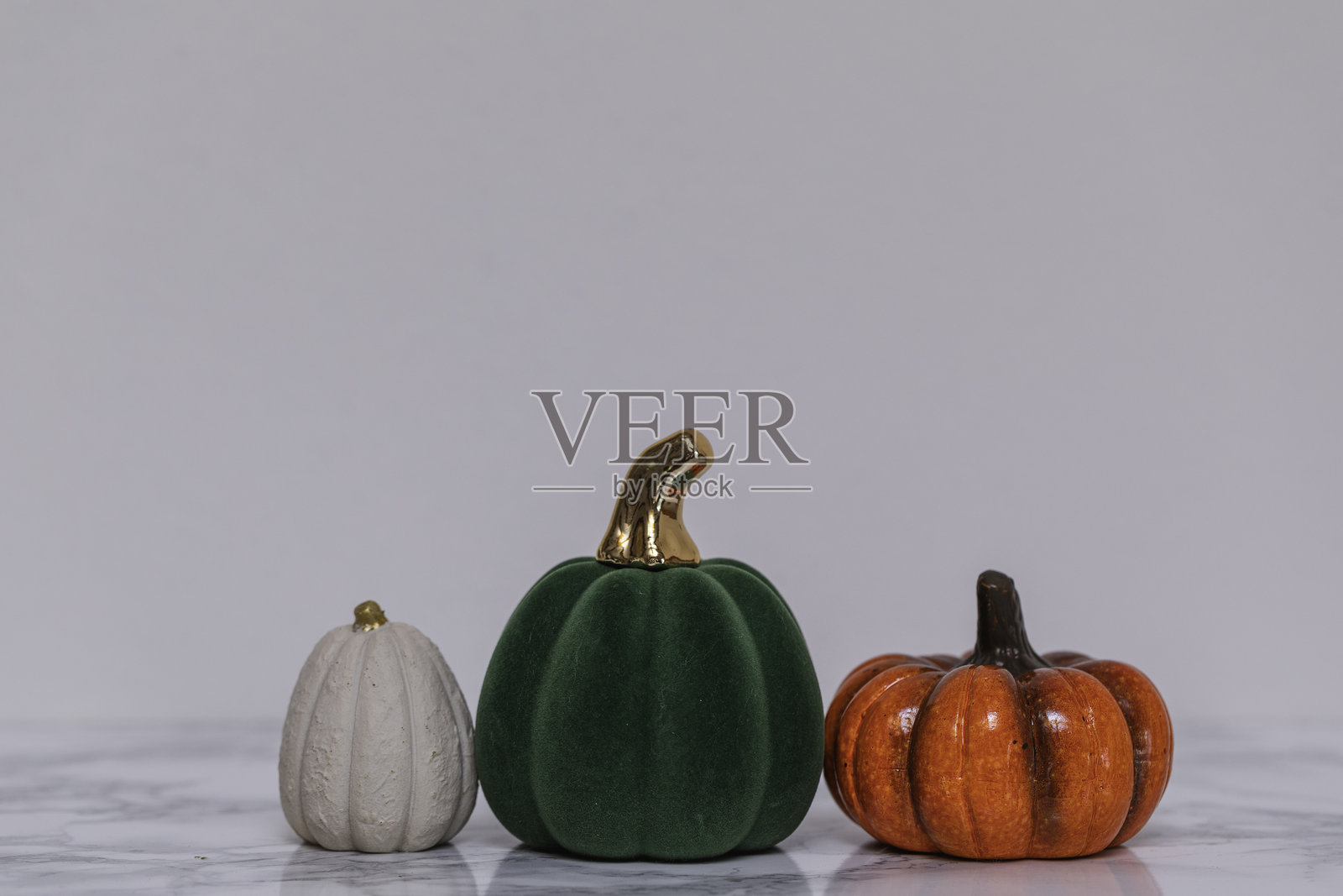 秋季假日装饰场景,配有质感奶油色的装饰南瓜、奢华的绿色天鹅绒金色细节,以及光亮的橙色陶瓷,置于大理石上,适合秋季室内风格和节日展示。照片摄影图片