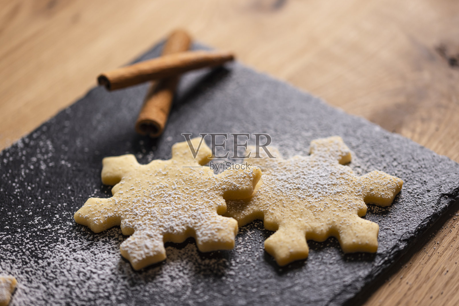 节日气氛的圣诞饼干,形状如雪花,搭配肉桂棒,摆放在深色石板盘上照片摄影图片