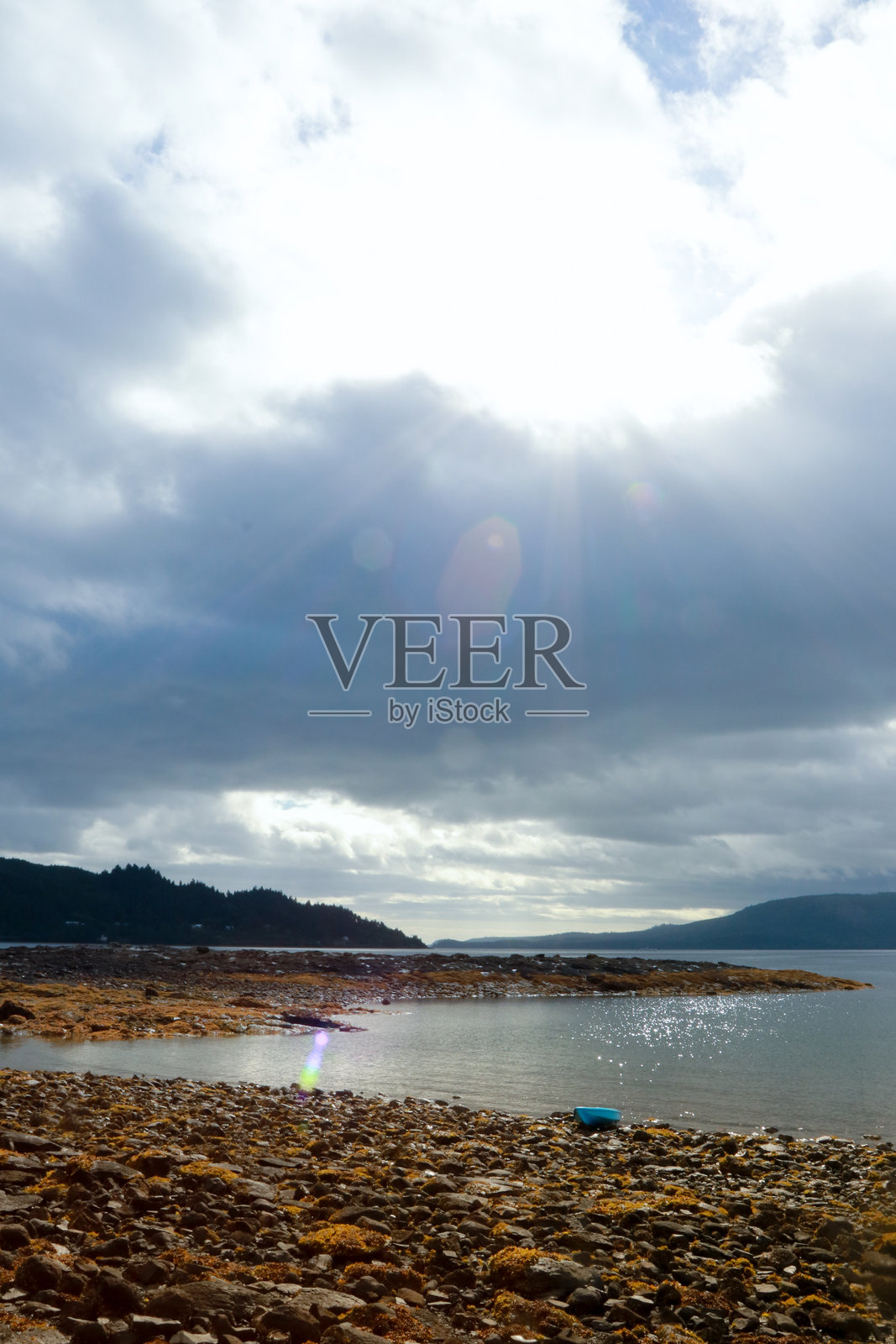 蓝色皮划艇静静地停靠在低潮时覆盖着海藻的岩石海岸上照片摄影图片