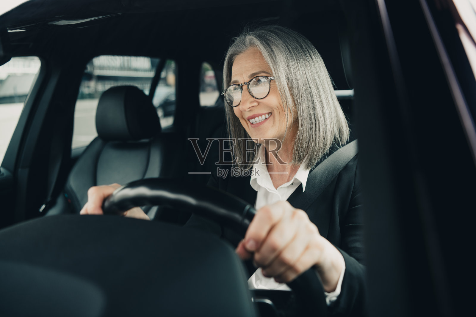 成功的成熟的女商人在阳光明媚的日子里,优雅专业地驾驶着汽车穿行于城市街区。照片摄影图片