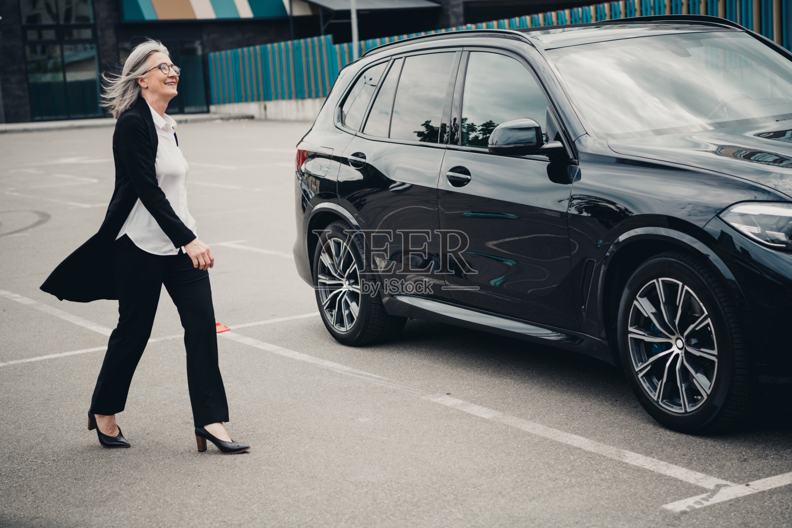 自信的成熟的女商人在城市环境中穿着正式服装,走在豪华车旁,阳光明媚。照片摄影图片