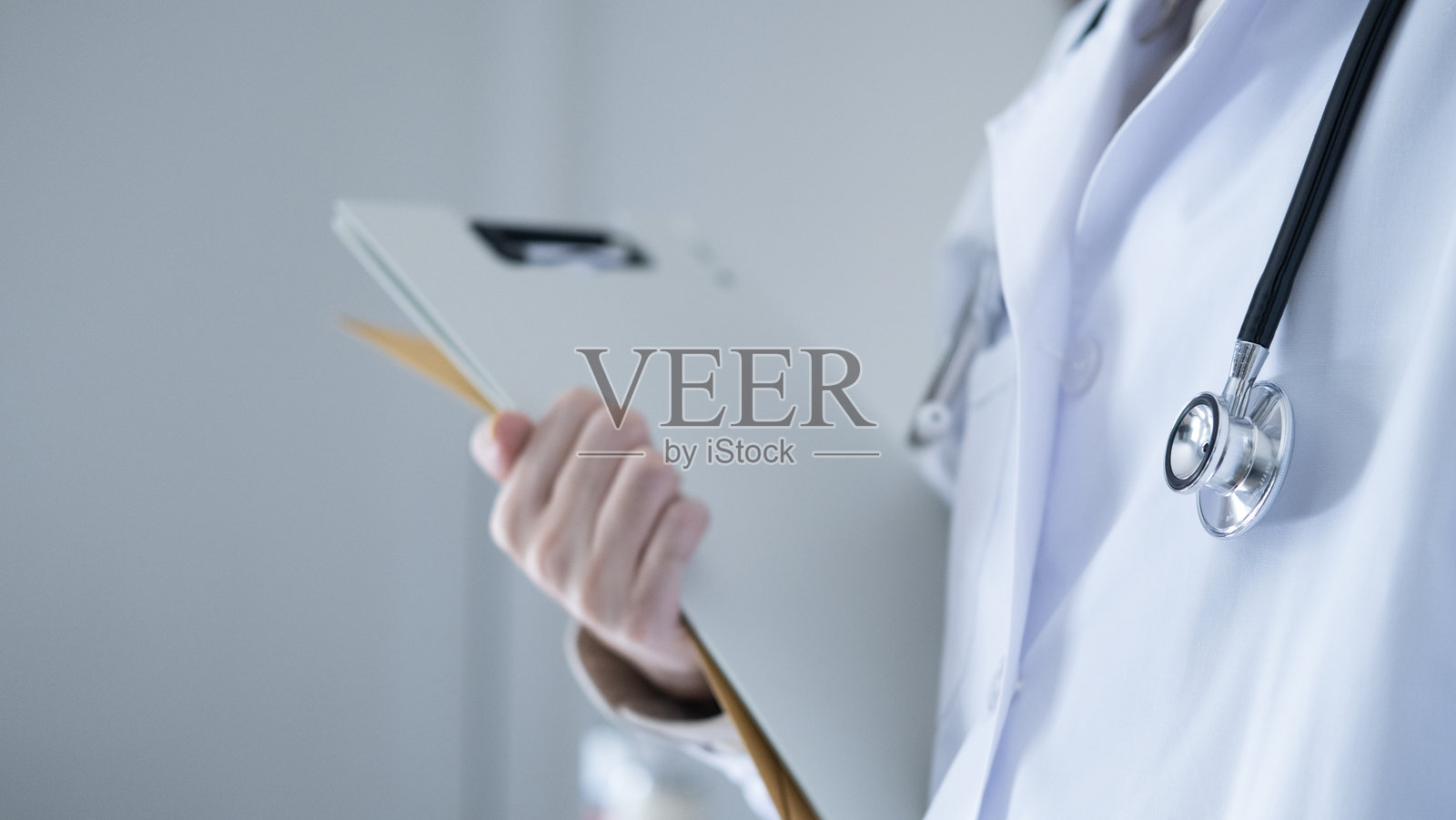 医生手持病历夹,佩戴听诊器的特写,代表医疗记录管理和专业医疗服务。照片摄影图片