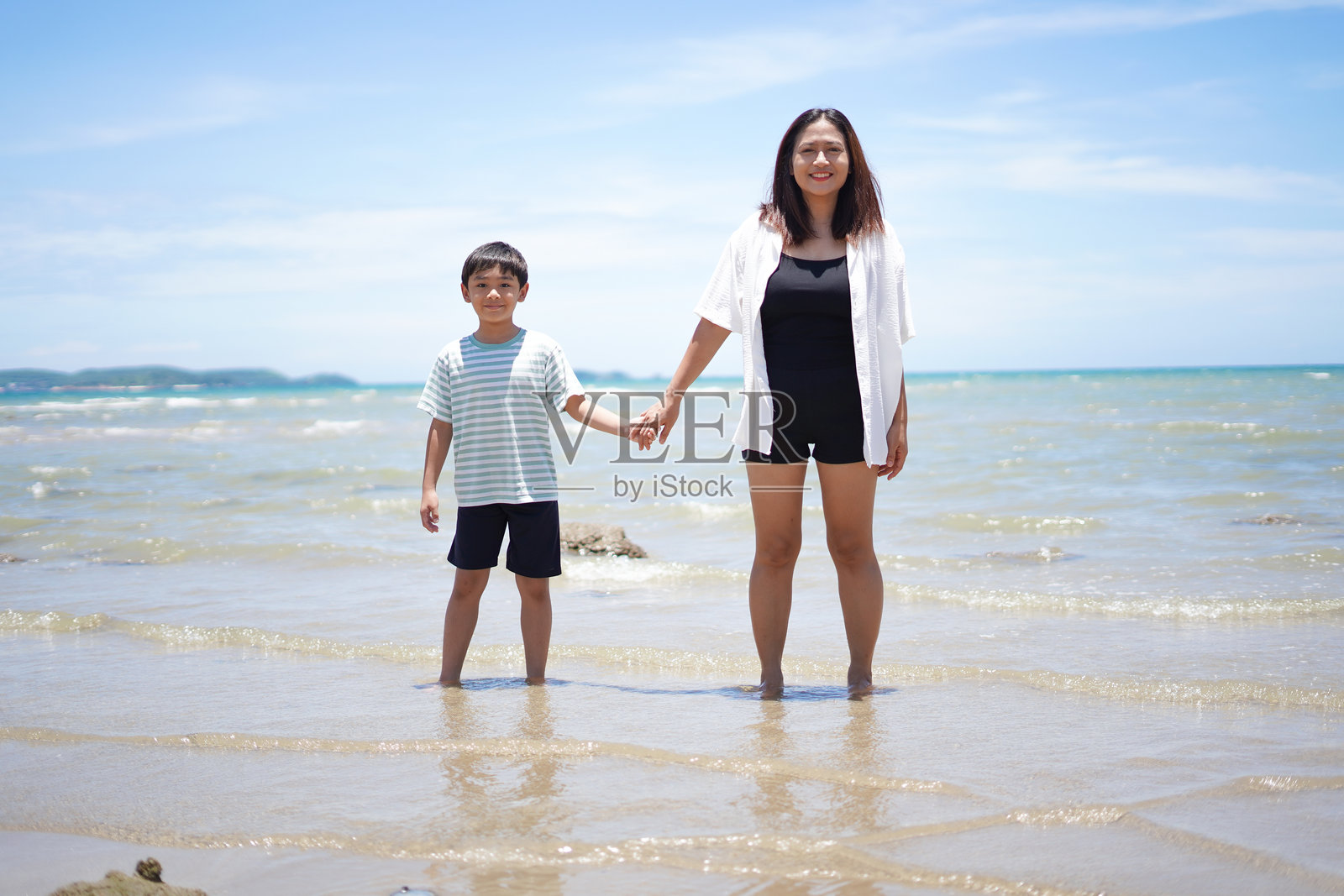母亲和儿子在海滩上牵手。照片摄影图片