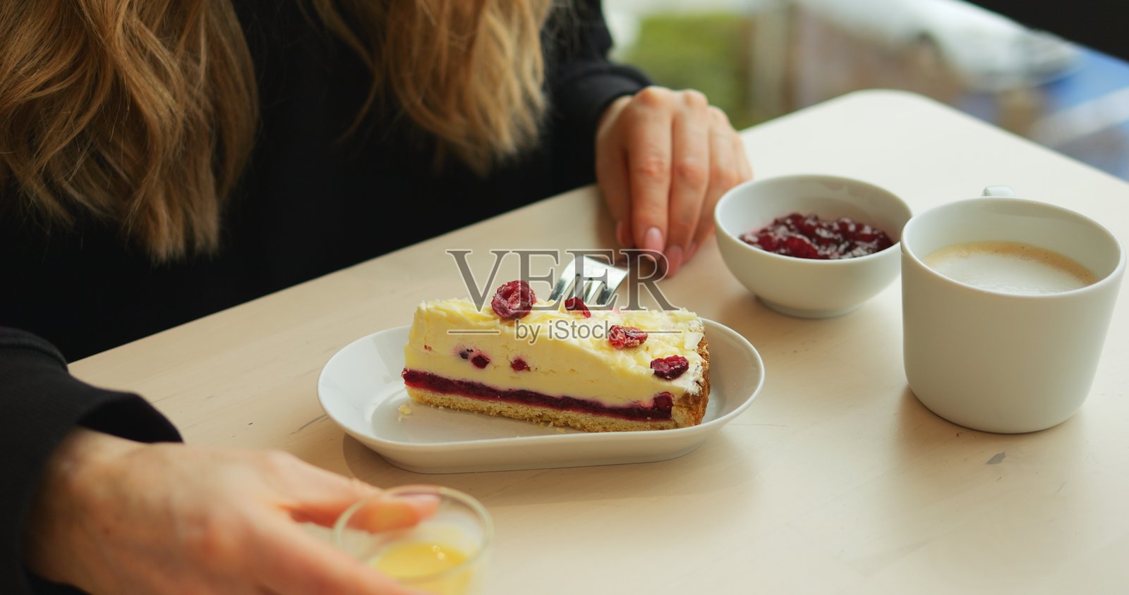 女人在咖啡馆的桌子上将奶油酱倒在放有浆果的芝士蛋糕上照片摄影图片