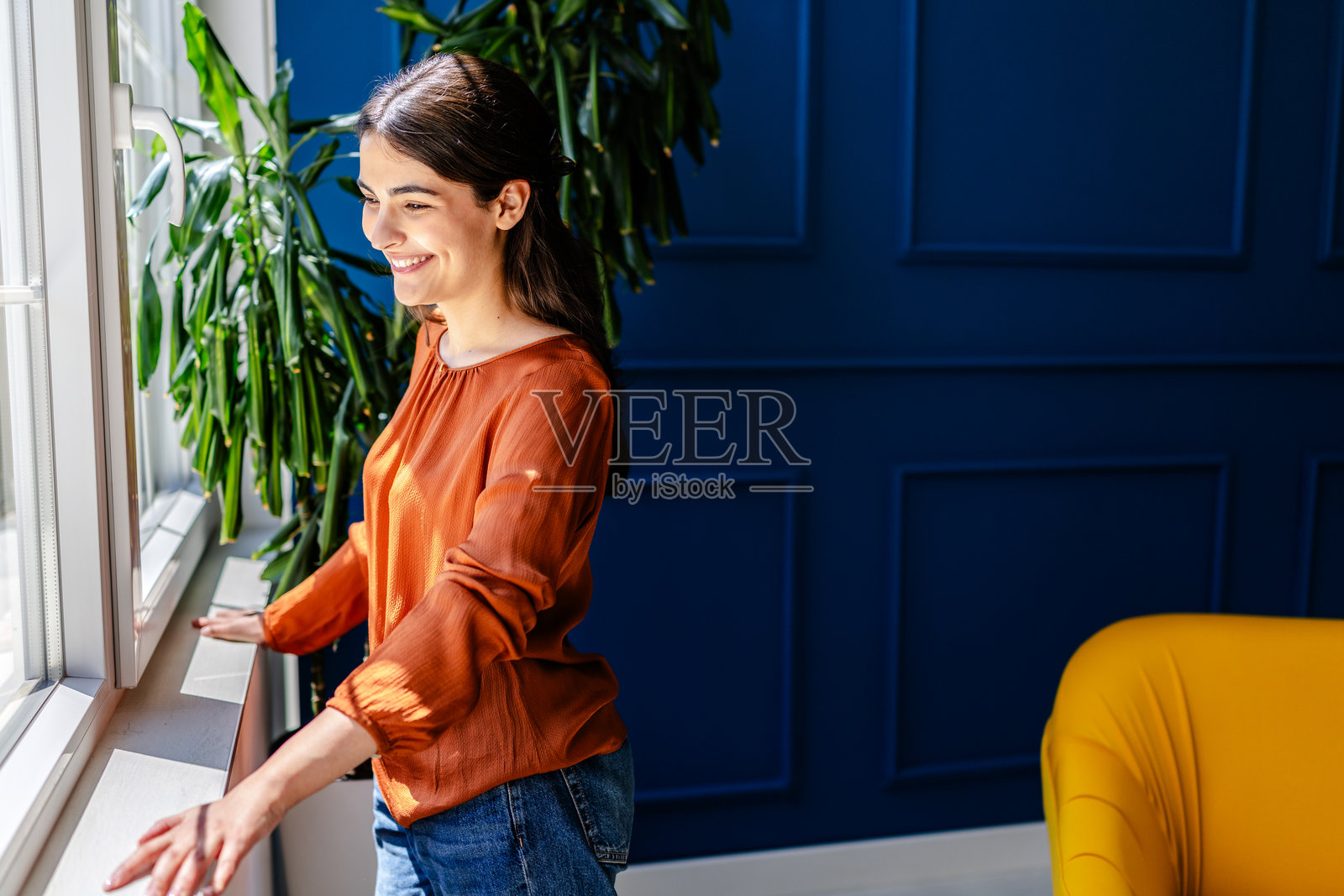 年轻女性在明亮的自然光照射下,微笑着享受舒适的客厅时光。照片摄影图片