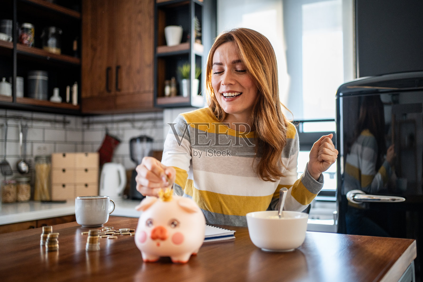 快乐的女人在吃早餐时把钱存进储蓄罐照片摄影图片