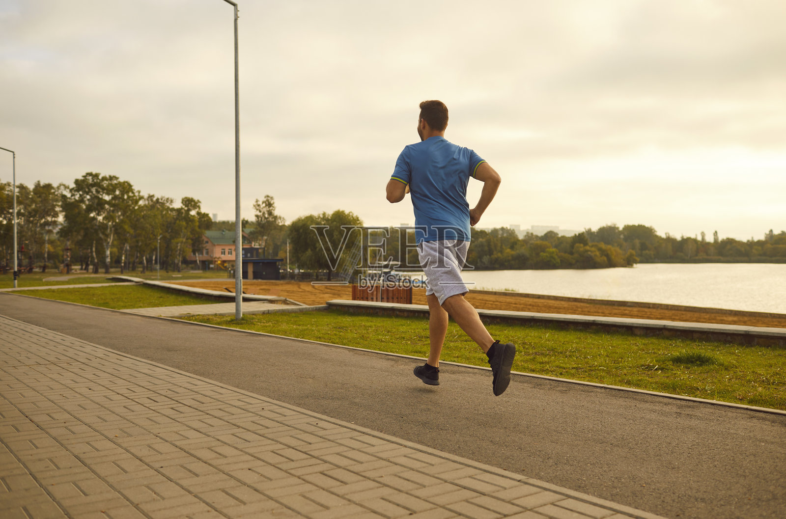 运动员从湖边的城市跑过,背影。照片摄影图片