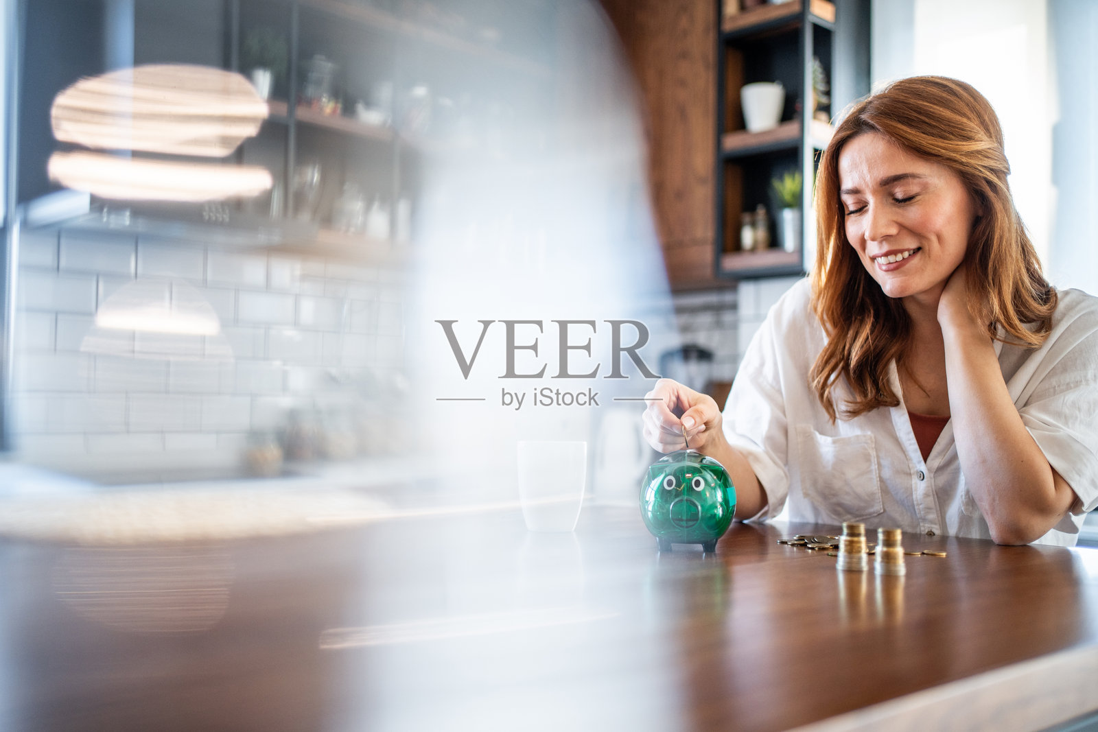 女人在家里把硬币放进储蓄罐里。照片摄影图片