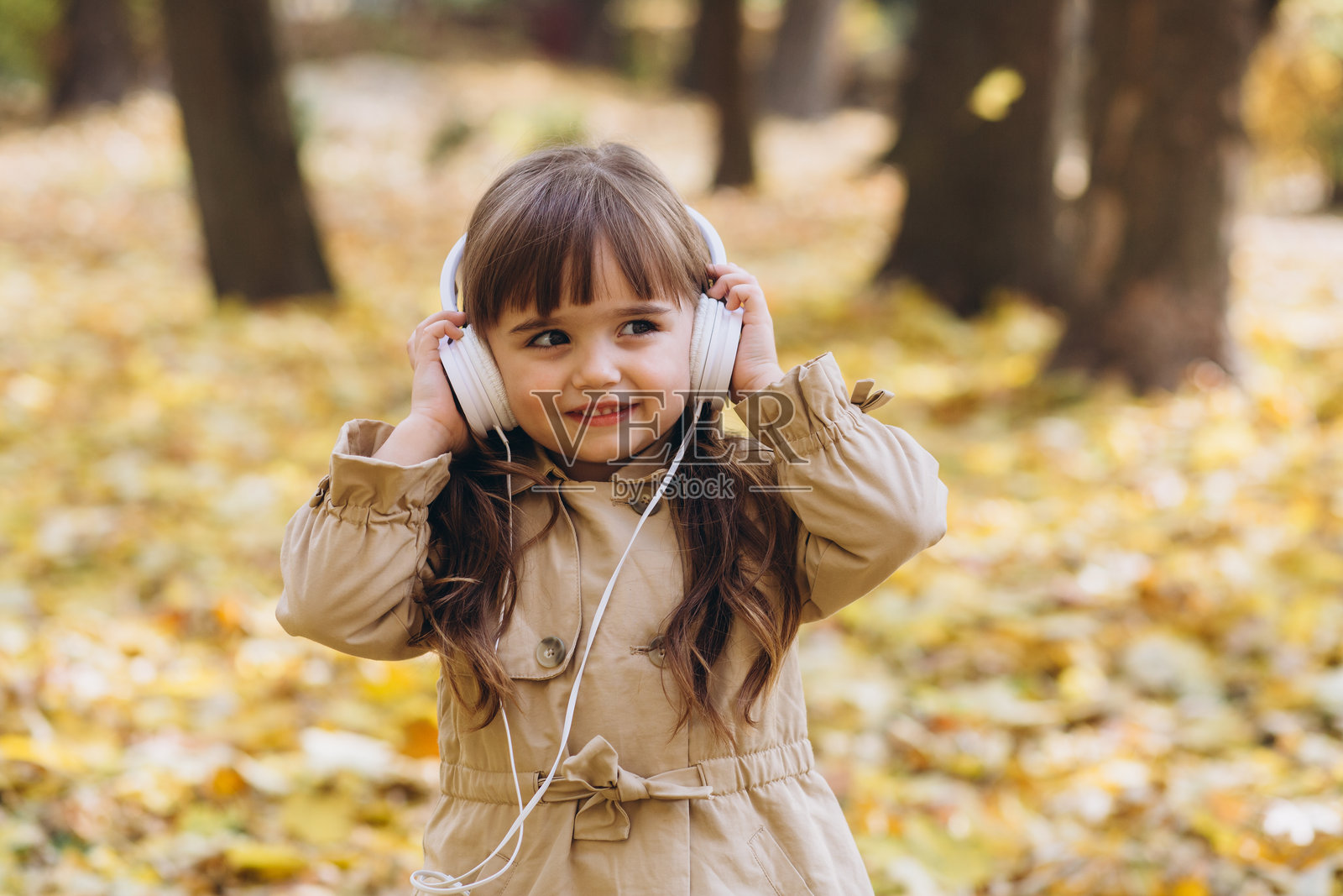 秋天公园里,一个快乐的小女孩戴着耳机听音乐的肖像照片摄影图片