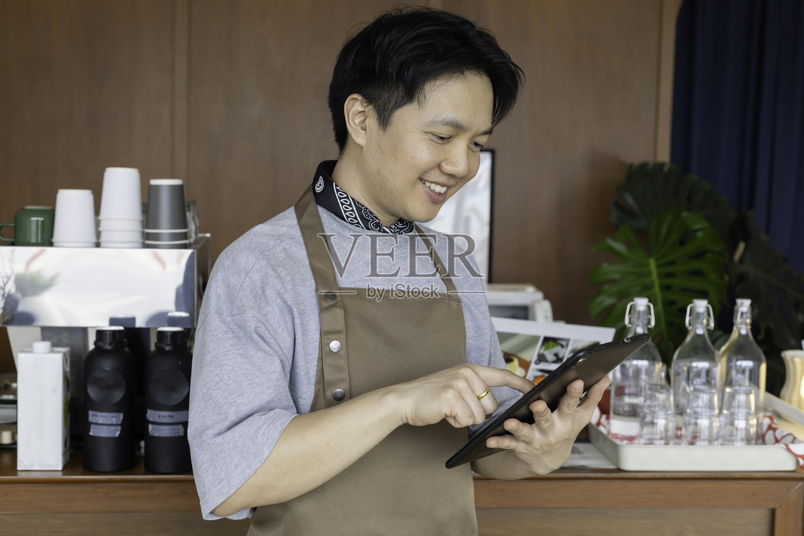 快乐的亚洲咖啡师,作为小企业主,在现代咖啡馆使用平板电脑处理订单。咖啡店创业者利用科技管理运营。照片摄影图片