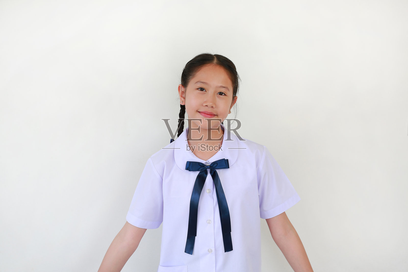 身穿校服的美丽亚洲学生女孩在白色摄影棚背景前站立。照片摄影图片