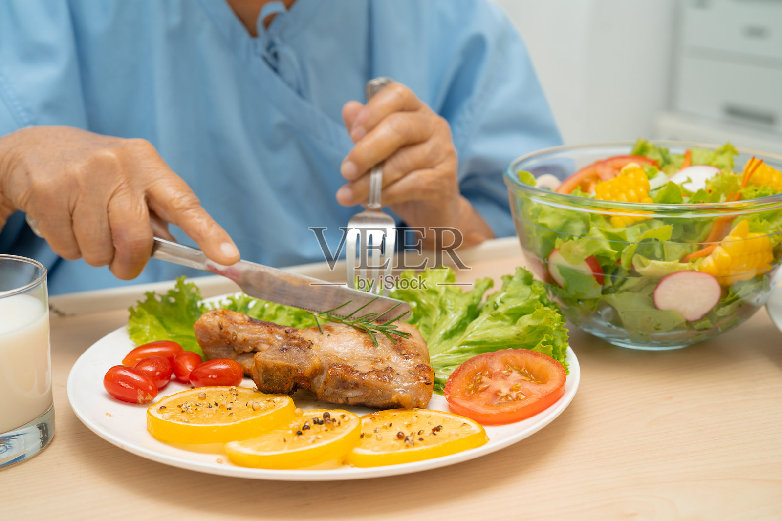 亚洲老年女性患者在医院吃猪排和蔬菜沙拉,享受健康饮食。照片摄影图片