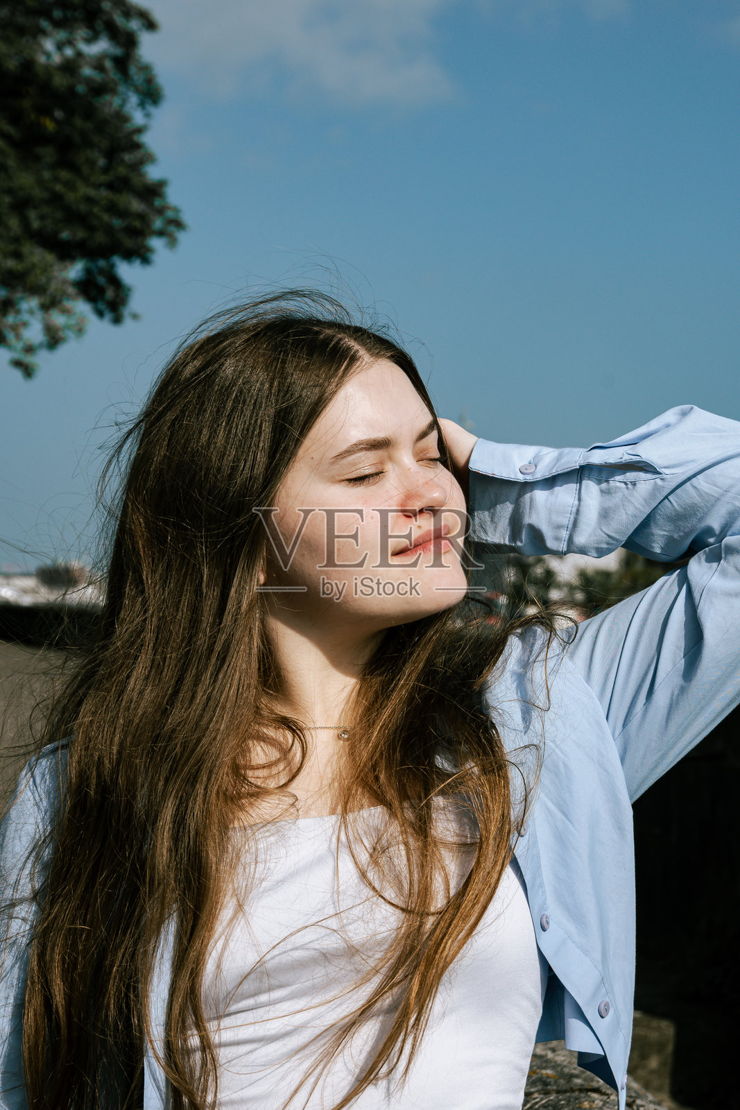 一位长发年轻女子站在树旁,闭着眼睛。照片摄影图片