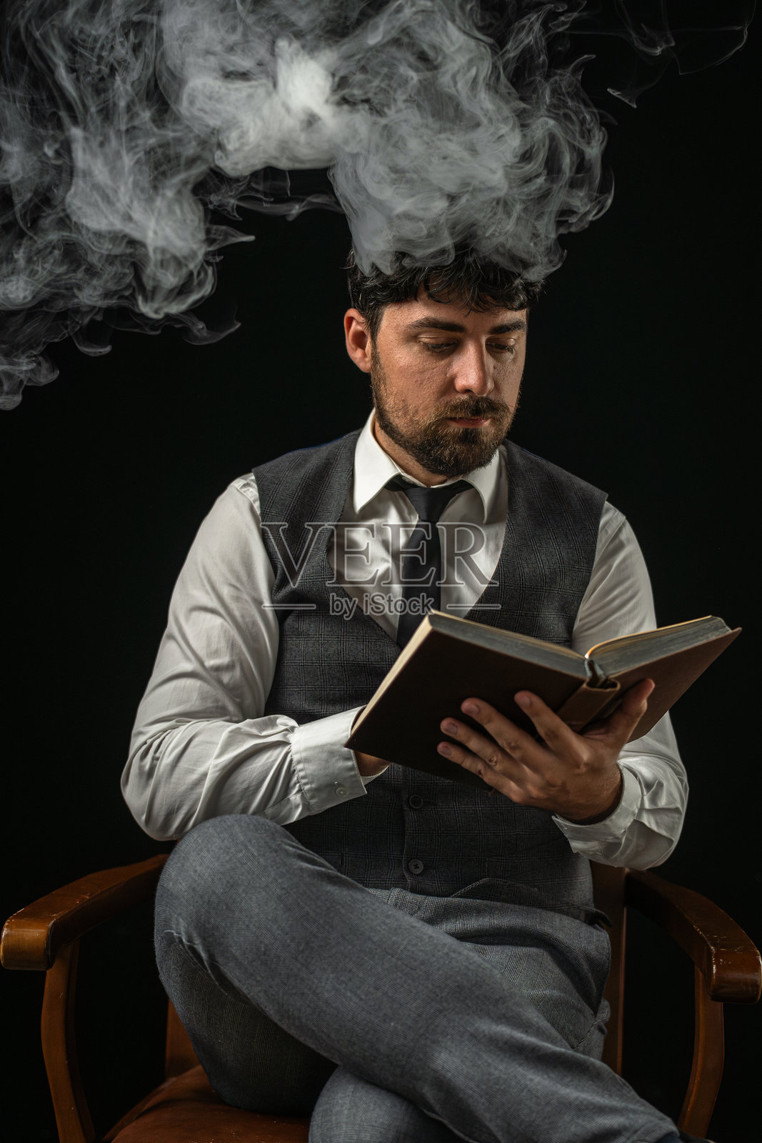 黑色背景下的男商人正在阅读一本书,周围弥漫着白色烟雾。照片摄影图片