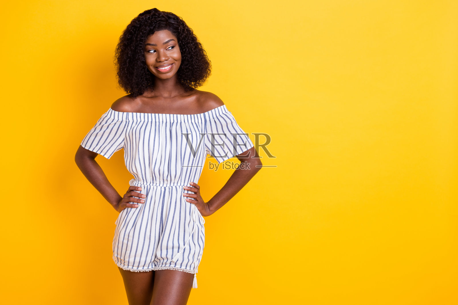 吸引人的快乐女孩双手叉腰摆姿势,背景为鲜艳的黄色,留有空白空间用于广告。照片摄影图片