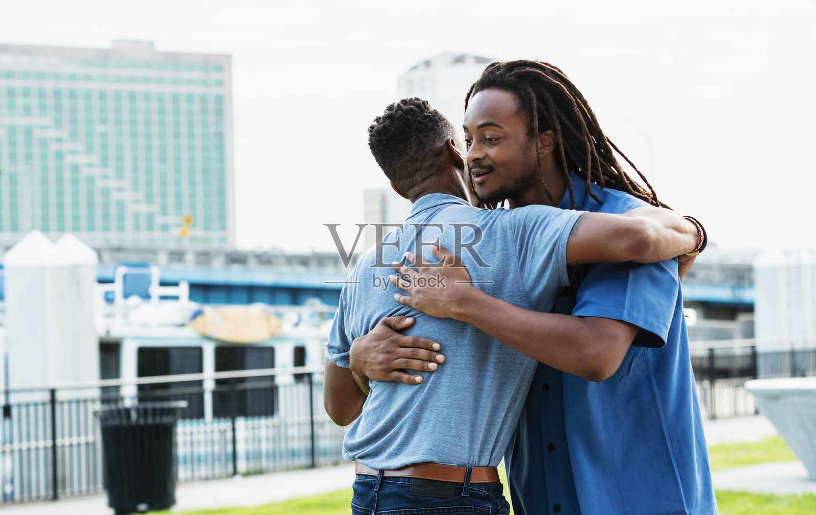 父亲和青少年儿子在城市公园拥抱照片摄影图片