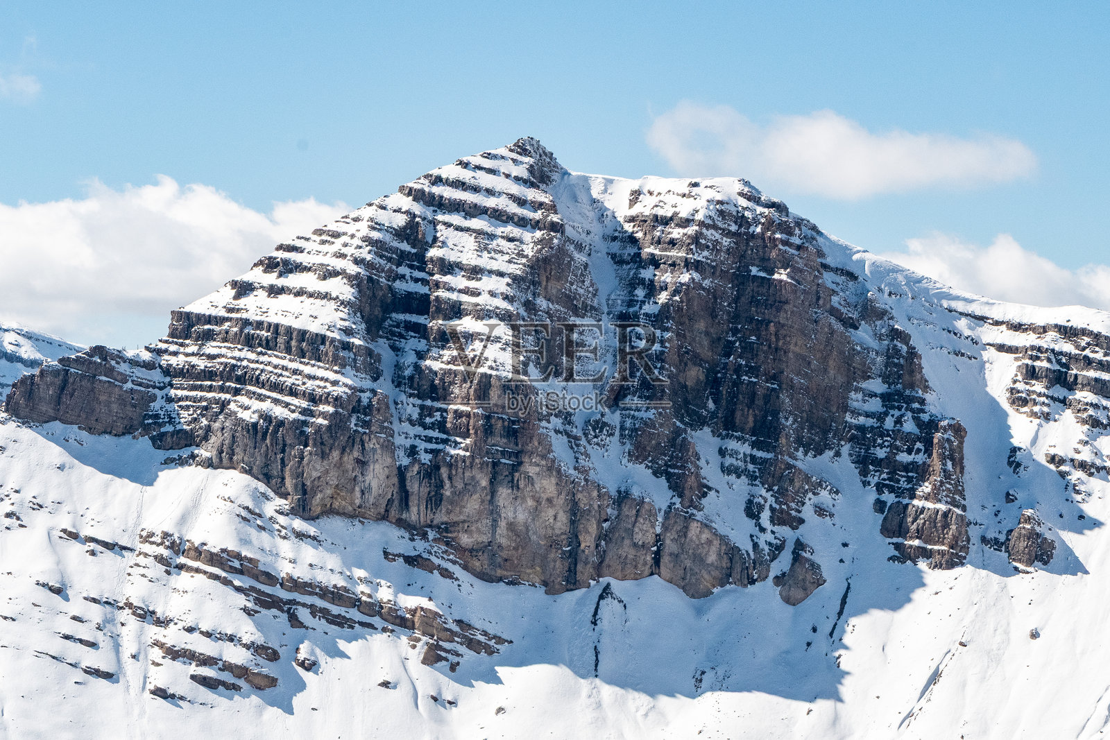 被雪覆盖的岩石山崖,暴露出分层的石头层,展示了深色岩石与明亮雪层之间的戏剧性对比照片摄影图片