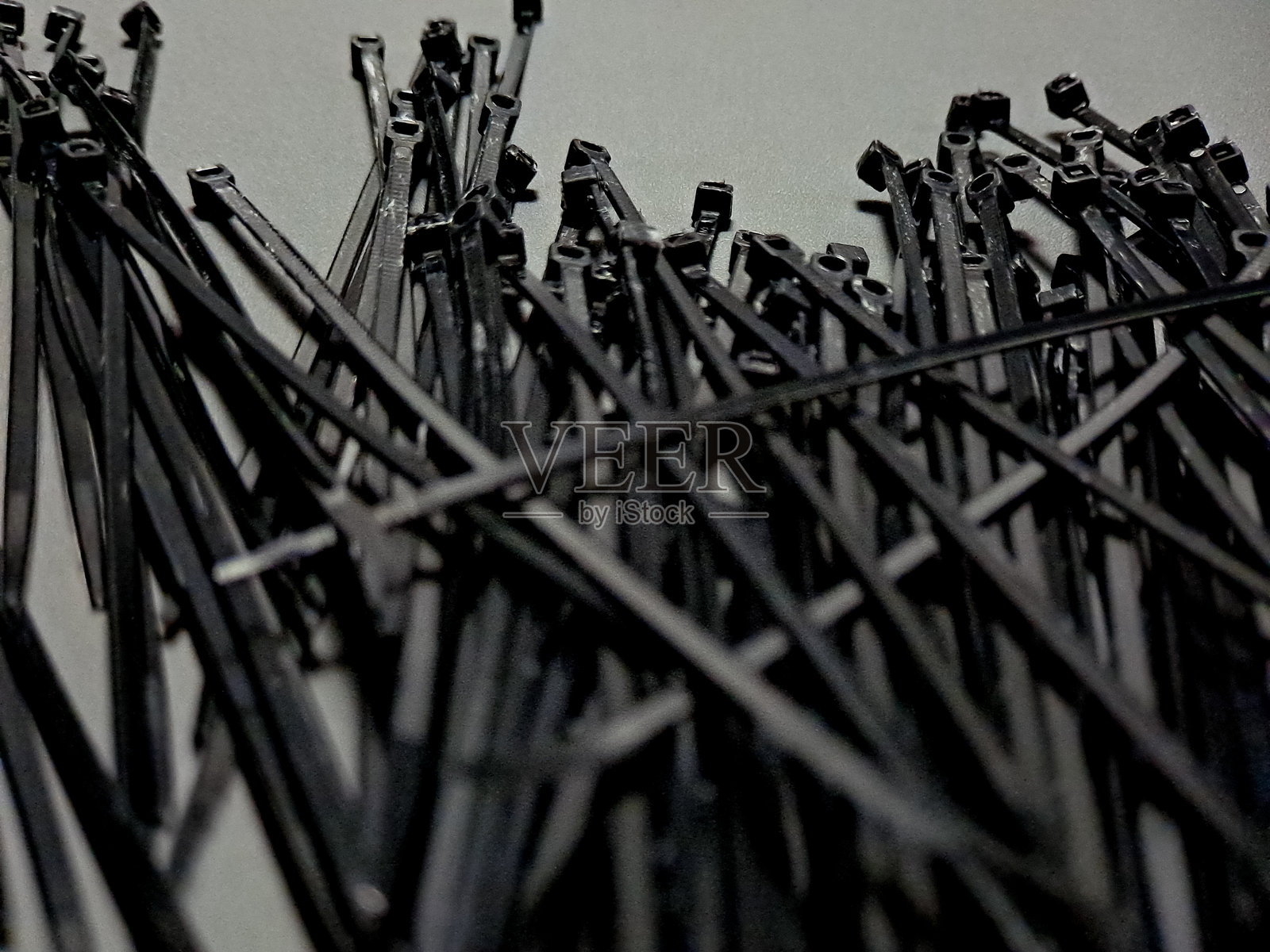 一堆黑色柔韧的尼龙扎带散落在浅灰色背景上,形成一种混乱却有序的纹理图案,展现出工业视觉魅力。照片摄影图片