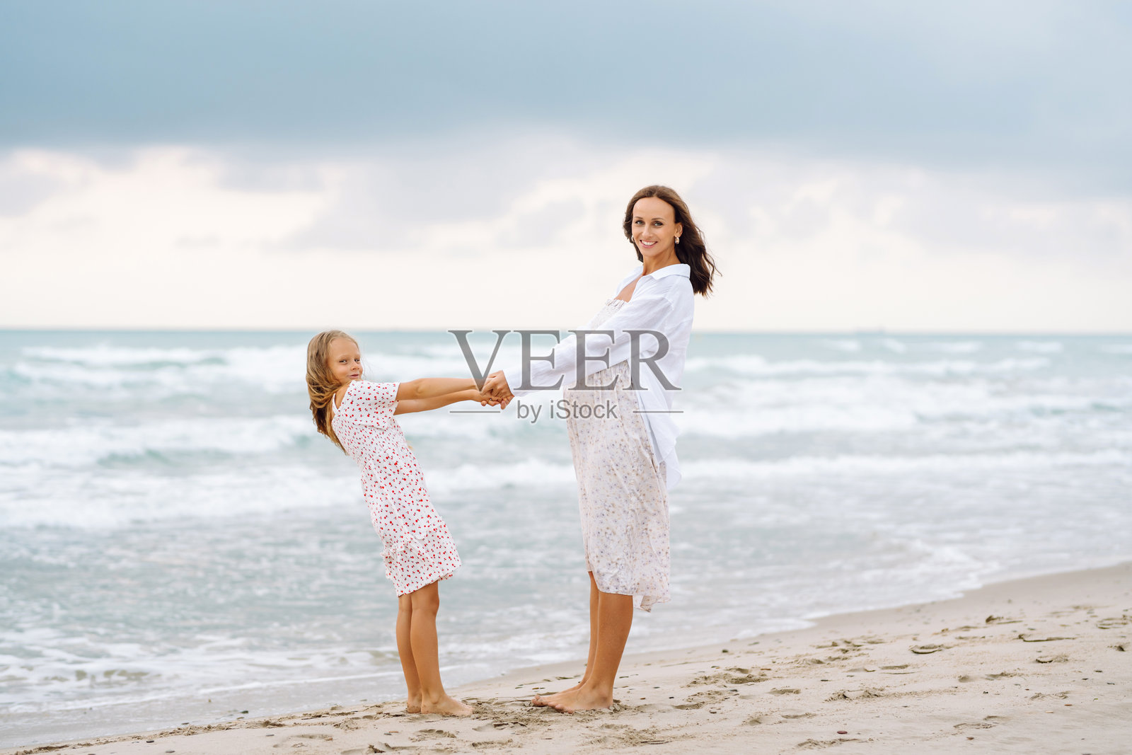 一位美丽的孕妇与一个可爱的女孩在海边共度时光。照片摄影图片