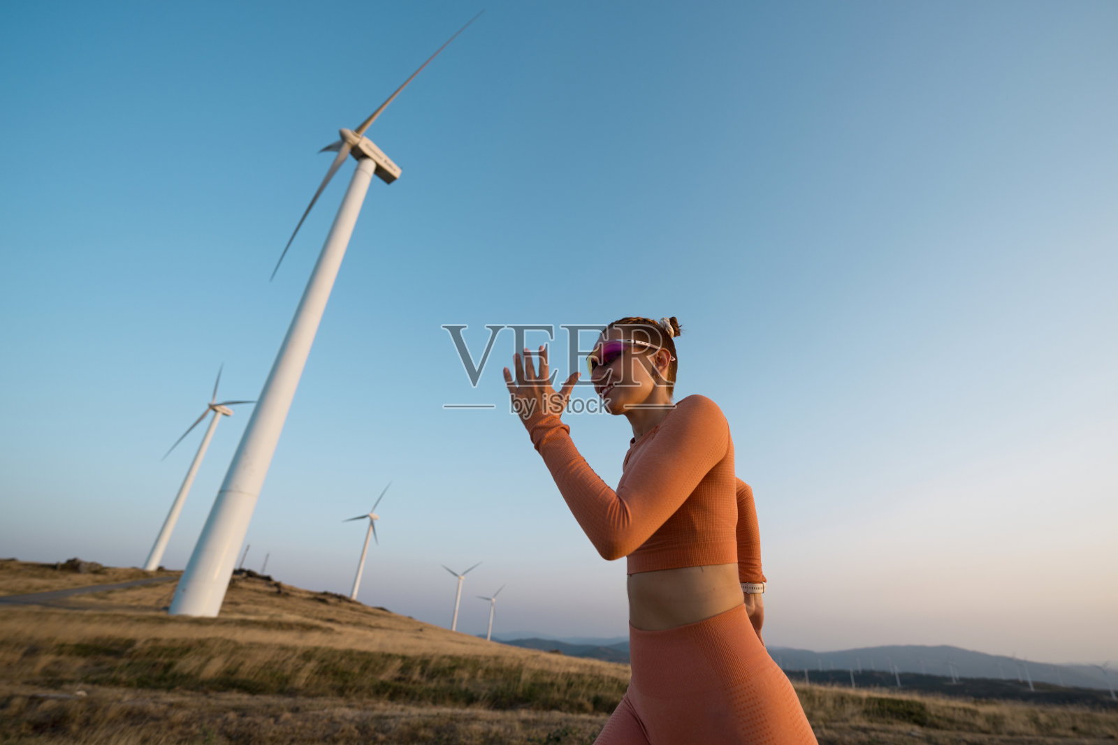 年轻的女运动员在风力发电机旁的田野上奔跑照片摄影图片