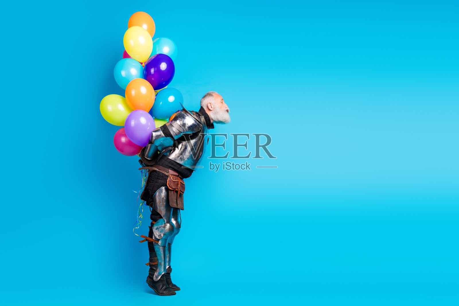 穿着中世纪骑士盔甲的老年男子在蓝色背景前手持五彩气球照片摄影图片