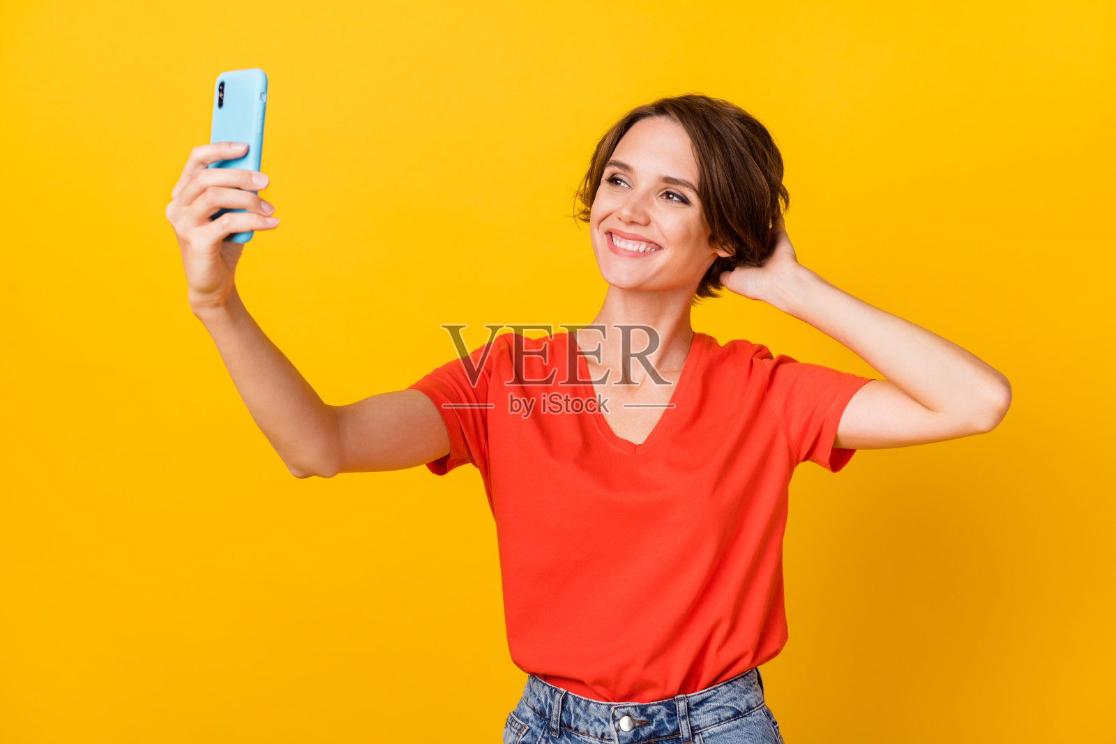 漂亮积极的女士自拍,手触头发,露出灿烂的微笑,背景为黄色。照片摄影图片