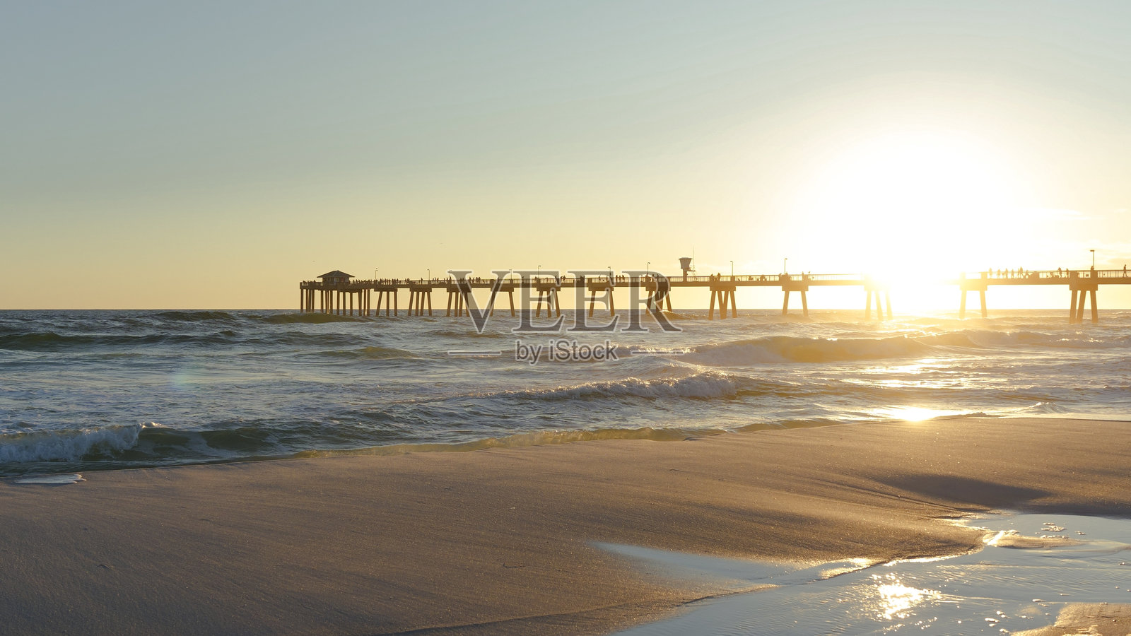 日落时分,海滩上有人漫步,背景是码头,营造出宁静的海岸氛围照片摄影图片